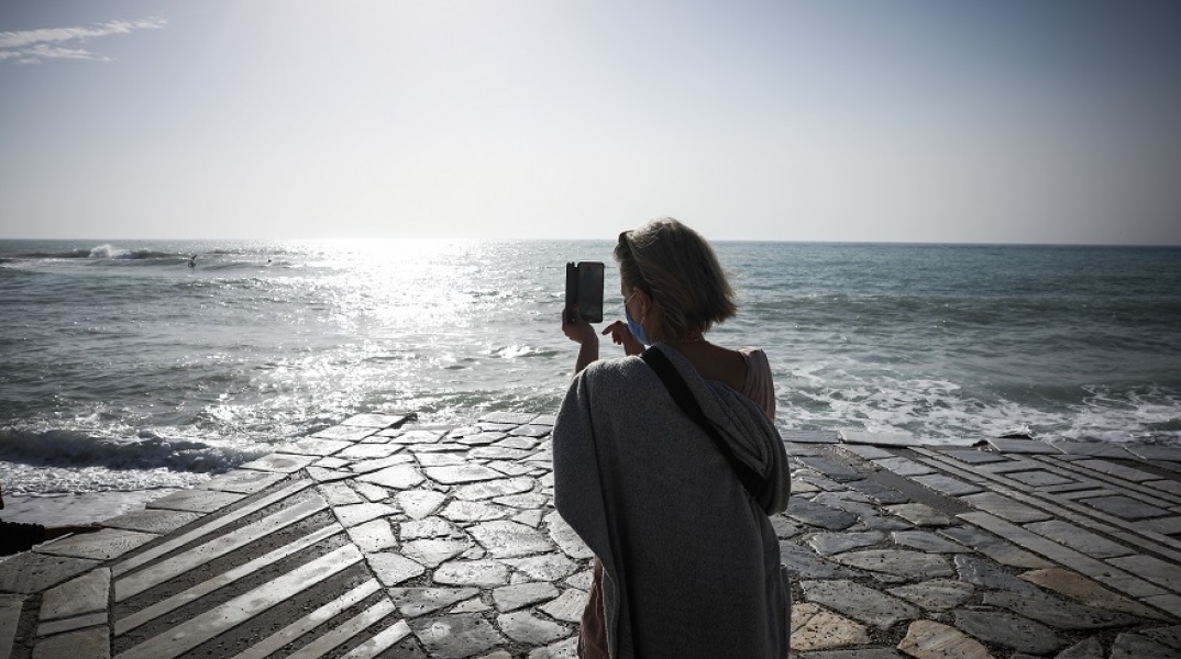 Γυναίκα με μάσκα κάνει βόλτα στη θάλασσα και φωτογραφίζει