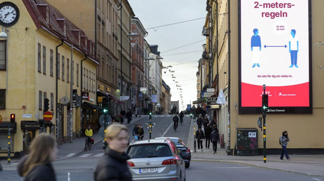 Σουηδία - Κορωνοϊός: Πολίτες χωρίς μάσκες στη Στοκχόλμη, με την ενημερωτική πινακίδα να αναφέρεται στην τήρηση απόστασης τουλάχιστον 2 μέτρων