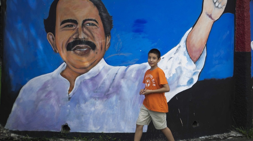 Παιδί κοιτάζει την κάμερα φωτογράφου με φόντο ένα γκράφιτι που απεικονίζει τον Ντανιέλ Ορτέγκα στη Νικαράγουα