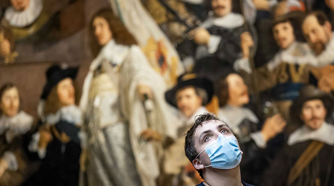Άμστερνταμ - Rijksmuseum: Νεαρός με μάσκα για τον κορωνοϊό με φόντο τον πίνακα «Νυχτερινή περίπολος» του Ολλανδού ζωγράφου Ρέμπραντ