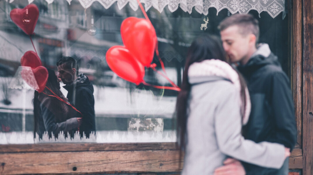 Ζευγάρι μπροστά σε βιτρίνα κρατάει μπαλόνια σε σχήμα καρδιάς