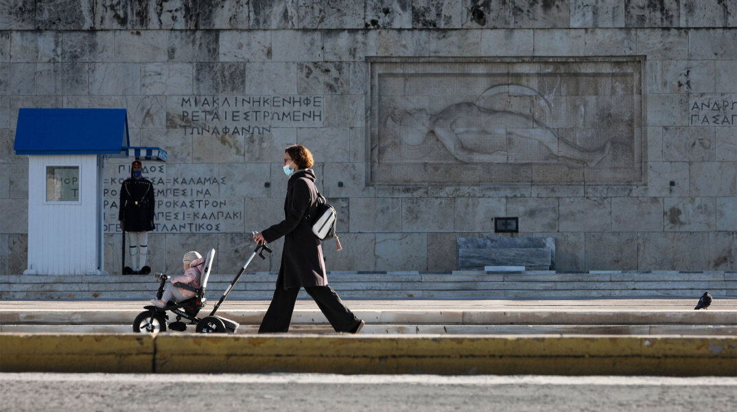 Κορωνοϊός στην Αττική: Μητέρα με το μωρό της, φορώντας μάσκα για Covid-19, περνά μπροστά από το Μνημείο του Αγνώστου Στρατιώτη στο Σύνταγμα