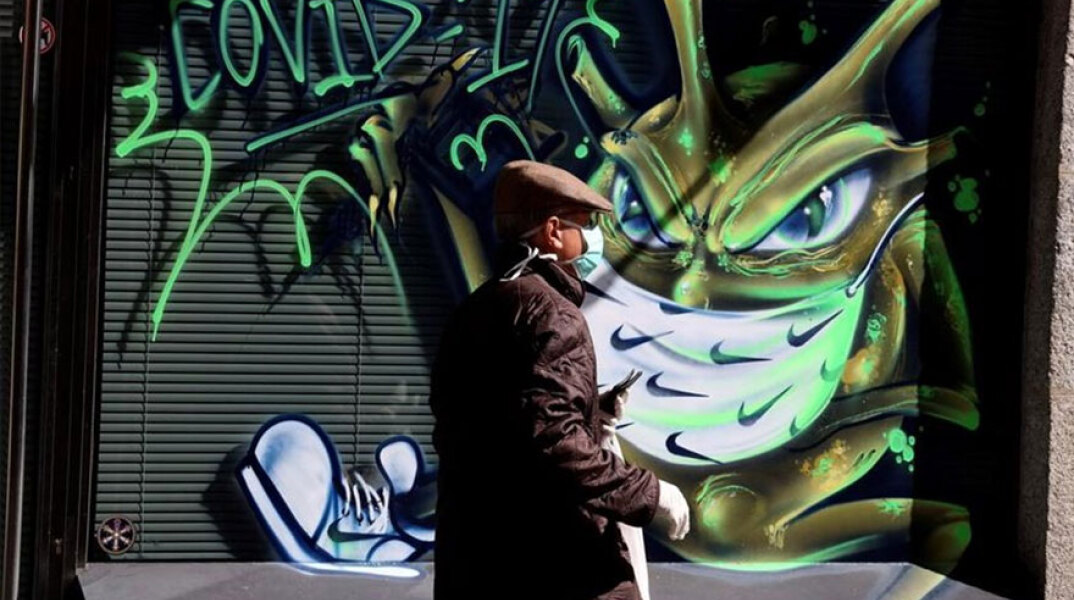 Άνδρας με μάσκα περνά μπροστά από γκράφιτι για τον κορωνοϊό