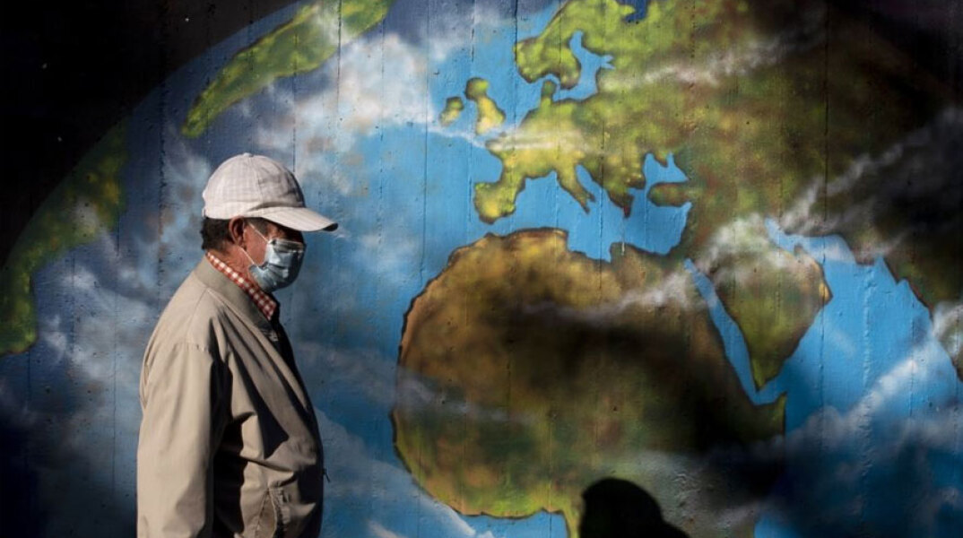 Άνδρας με προστατευτική μάσκα για τον κορωνοϊό περνά μπροστά από γκράφιτι με τον παγκόσμιο χάρτη της Γης