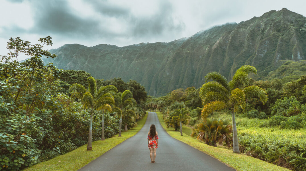 Γυναίκα στέκεται στη μέση ενός δρόμου με φόντο πράσινα δαση