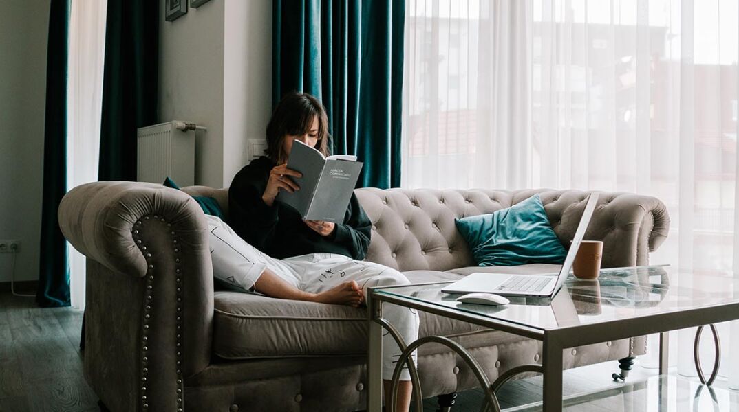 Κοπέλα που κάθεται στον καναπέ και διαβάζει βιβλίο