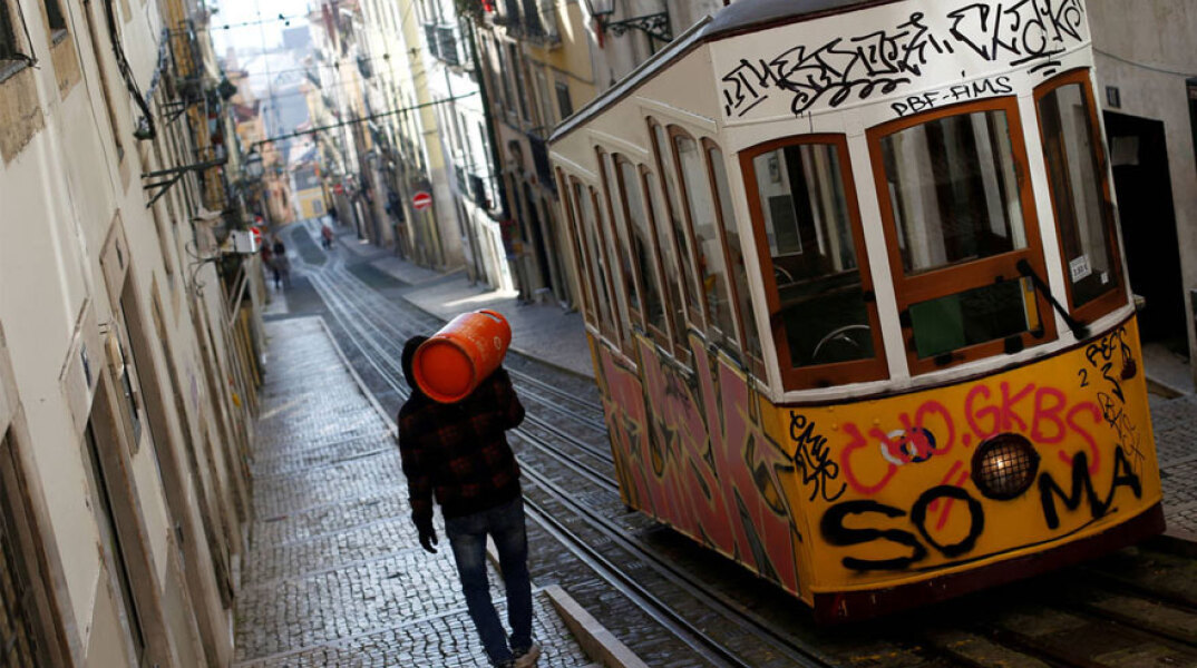 Πορτογαλία - Κορωνοϊός: Άνδρας κουβαλά φιάλη υγραερίου στην πλάτη δίπλα από συρμό του τραμ στη Λισαβόνα