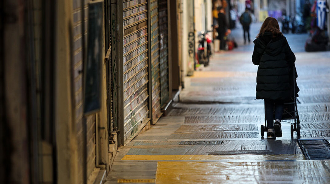 Lockdown στην Αττική: Γυναίκα περνά έξω από κλειστά καταστήματα