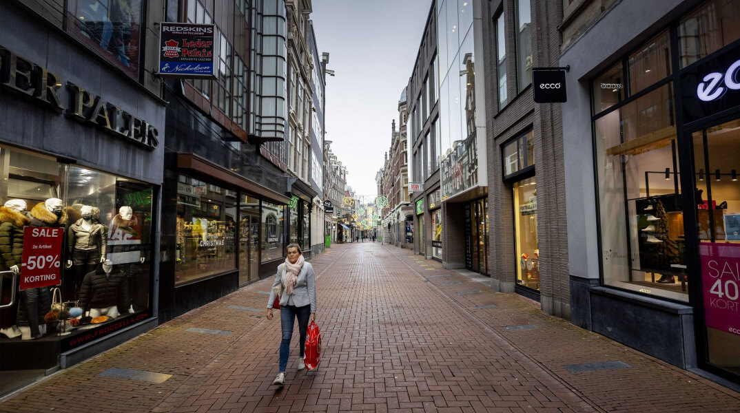 Ολλανδία - Lockdown: Γυναίκα περπατά σε εμπορικό δρόμο στο Άμστερνταμ