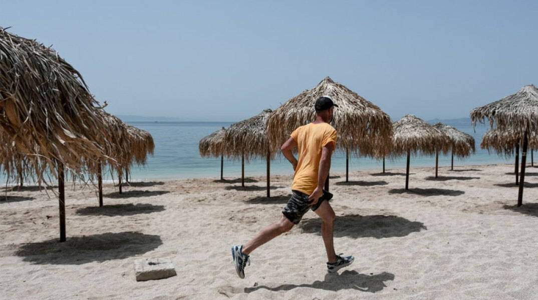 Άνδρας με μαγιό, αθλητικά παπούτσια και καπέλο τρέχει σε παραλία