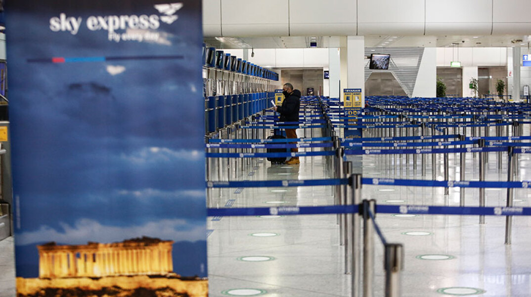 Διεθνές αεροδρόμιο «Ελευθέριος Βενιζέλος» στην εποχή του κορωνοϊού - Ταξιδιώτης με μάσκα ετοιμάζεται να δώσει τη βαλίτσα στο γκισέ και να τσεκάρει το εισιτήριό του