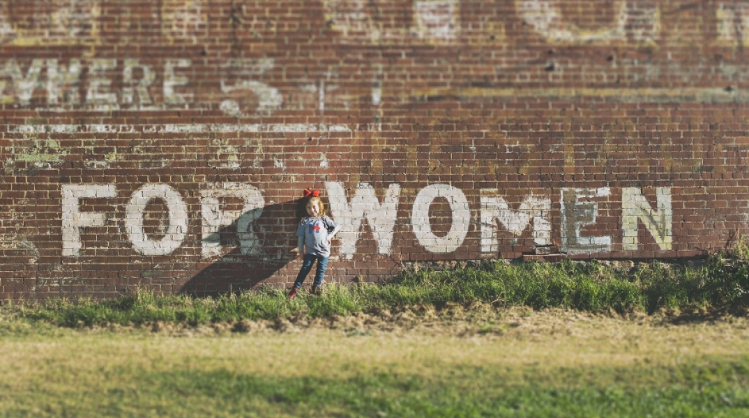 Κοριτσάκι κάθεται μπορστά από τοίχο με φκράφιτι «For Women»