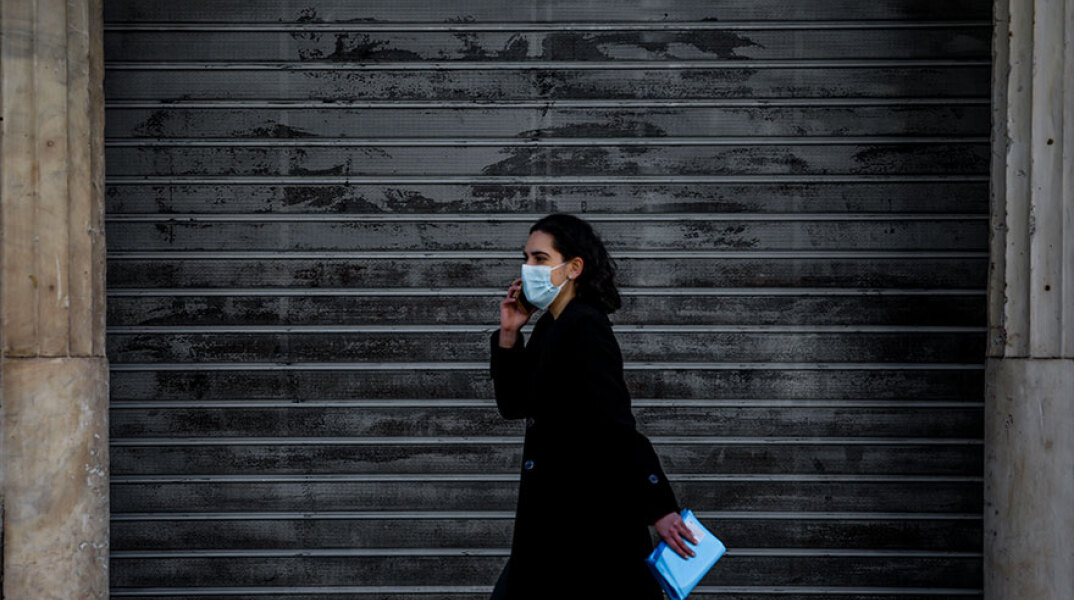 Αττική - Lockdown: Κοπέλα με μάσκα για τον κορωνοϊό μπροστά από κλειστό κατάστημα στην Αθήνα