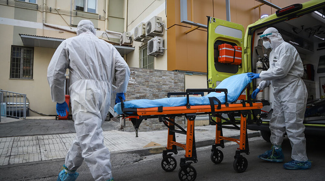 Υγειονομικοί του ΕΚΑΒ με προστατευτικές στολές ετοιμάζονται να μεταφέρουν σε φορείο νέο ασθενή με κορωνοϊό