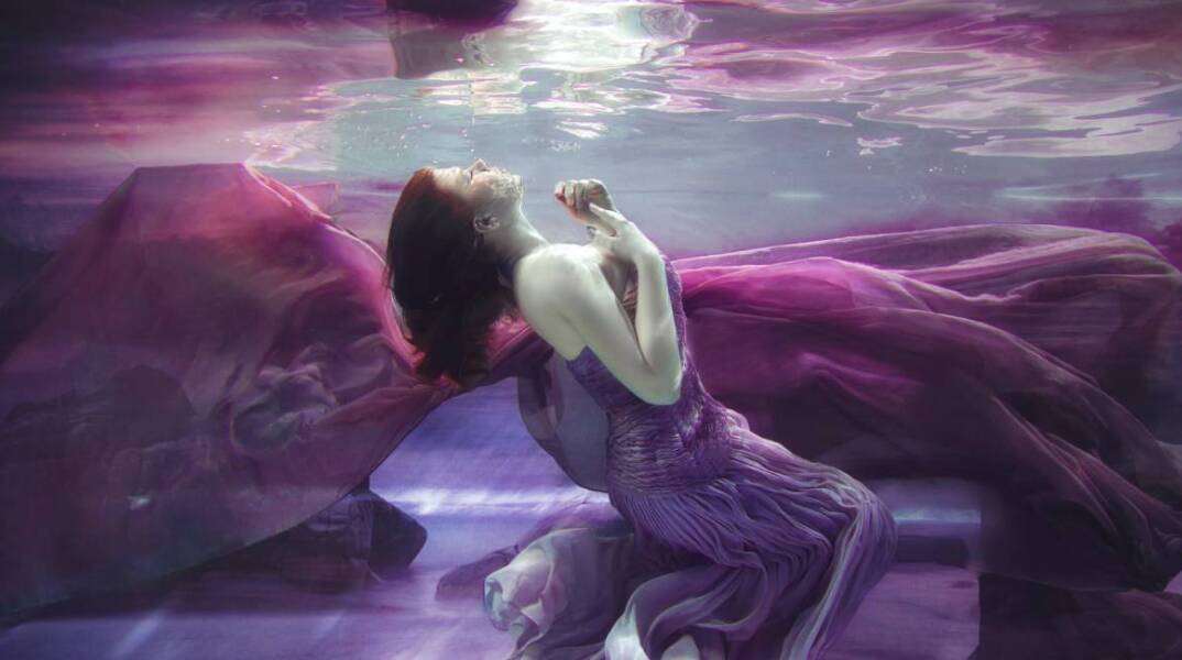 Γυναίκα με μοβ φόρεμα φωτογραφίζεται κάτω από το νερό