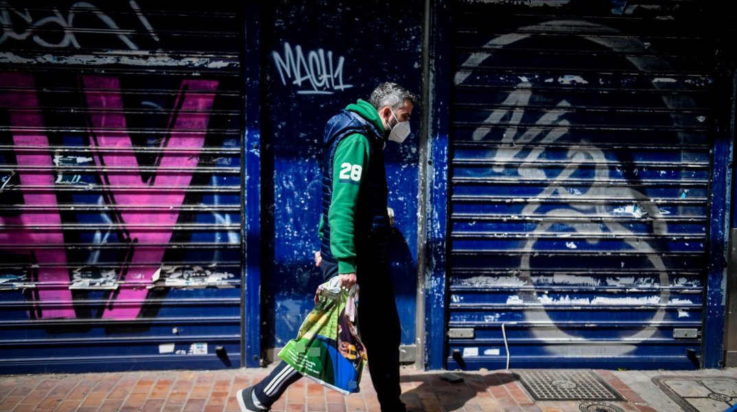 Πολίτης με μάσκα περπατά μπροστά από κλειστό κατάστημα