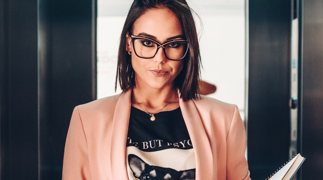 Γυναίκα στο ασανσέρ με καρέ μαλί, γυαλιά μυωπίας, μαύρη μπλούζα και ροζ σακάκι