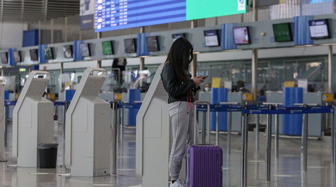 Αεροδρόμιο «Ελευθέριος Βενιζέλος»: Κοπέλα κοιτά το κινητό της μπροστά στον φωτεινό πίνακα για τις πτήσεις εσωτερικού - εξωτερικού