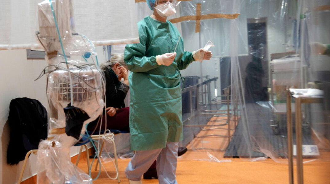 Υγειονομικός σε νοσοκομείο με προστατευτική στολή για τον κορωνοϊό διενεργεί τεστ για Covid-19 σε ηλικιωμένο άτομο
