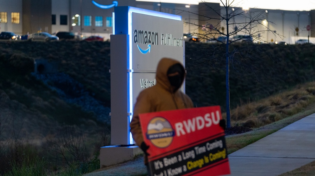 Εργαζόμενος κρατά πλακάτ έξω από αποθήκη της Amazon