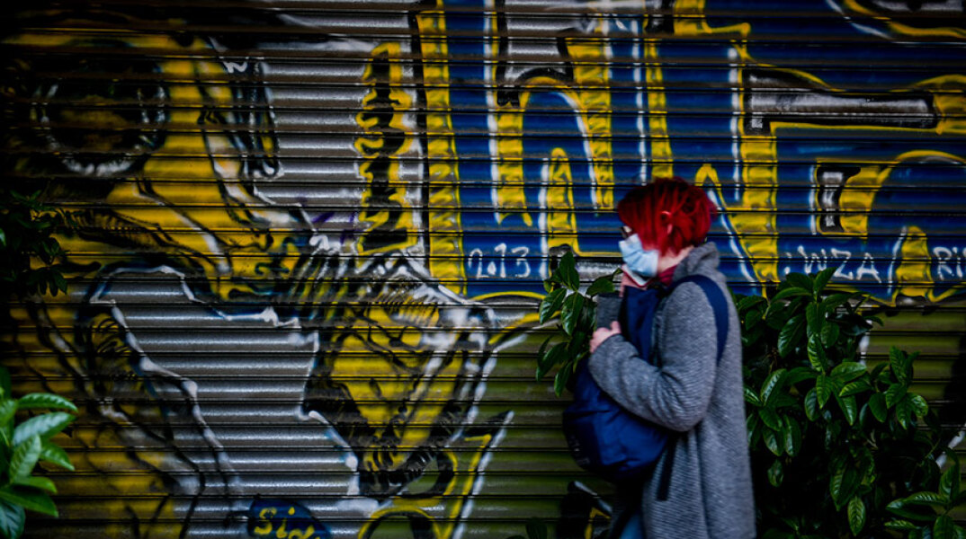 Αττική - Κορωνοϊός: Γυναίκα με μάσκα περνά μπροστά από γκράφιτι στο κέντρο της Αθήνας