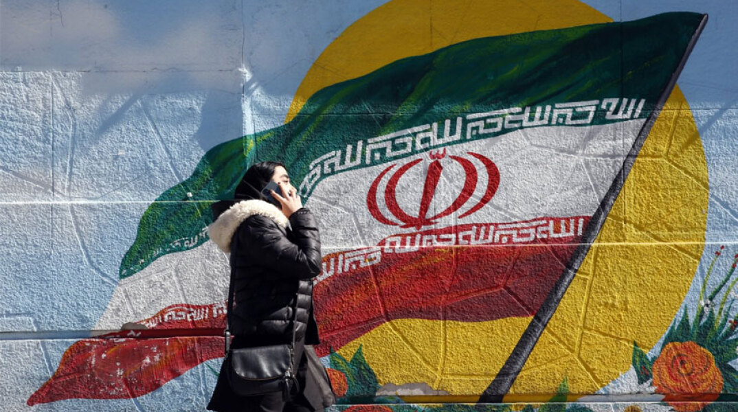 Ιρανή μιλά στο κινητό της τηλέφωνο περνώντας μπροστά από ένα γκράφιτι με τη σημαία του Ιράν στην πρωτεύουσα Τεχεράνη