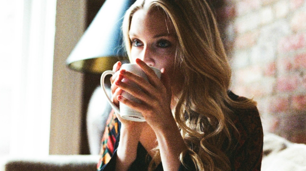 Γυναίκα με φλοράλ φόρεμα πίνει καφέ και διαβάζει βιβλίο