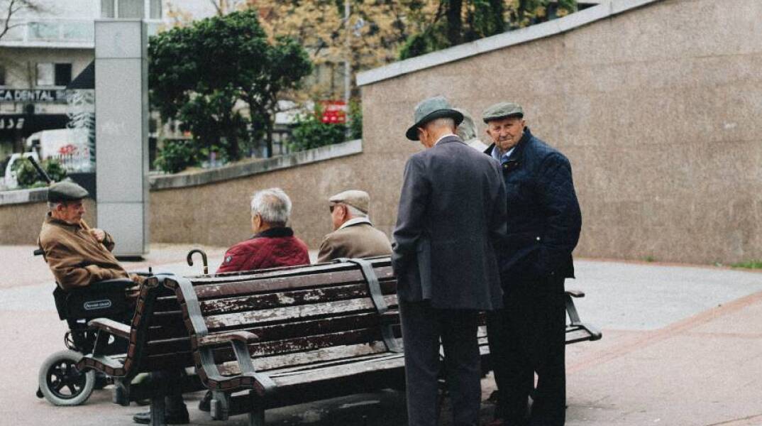 Ηλικιωμένοι άντρες στέκονται και συζητούν γύρω από ένα παγκάκι