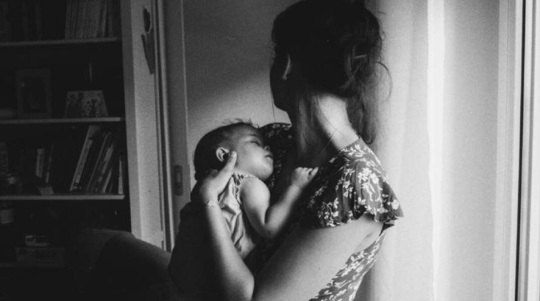 Ασπρόμαυρη φωτογραφία με μια μαμά που κρατάει στην αγκαλιά της ένα μωρό