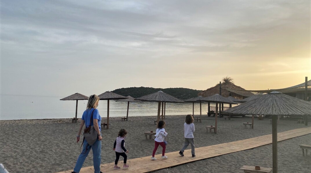 Γυναίκα περπατά σε παραλία με τρία παιδιά