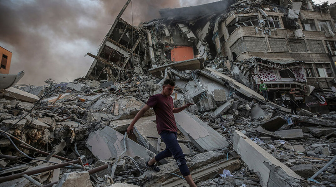 Παλαιστίνιος περπατά πάνω στα ερείπια κτιρίου που κατέρρευσε στη Λωρίδα της Γάζας μετά από αεροπορικό βομβαρδισμό του Ισραήλ