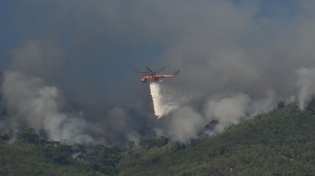 Μεγάλη φωτιά στην Κορινθία, με ελικόπτερο της Πυροσβεστικής να ρίχνει νερό πάνω από εστία της πυρκαγιάς που καίει το δάσος