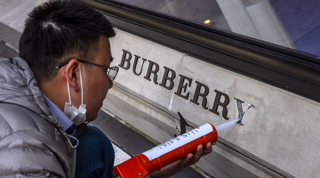 Ένας άντρας επισκευάζει κατεστραμμένο λογότυπο μπροστά από το κατάστημα Burberry στη Σαγκάη της Κίνας, στις 26 Μαρτίου 2021.