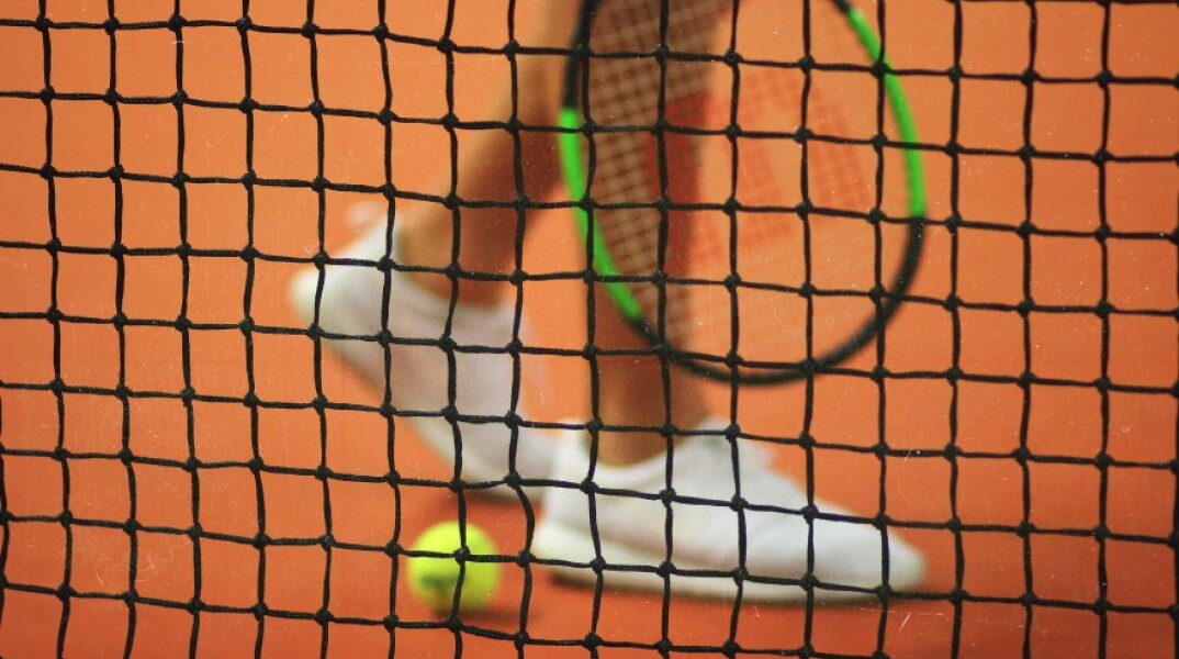 Παίκτρια του τένις κρατάει ρακέτα πίσω από το φιλέ©unsplash-John Fornander