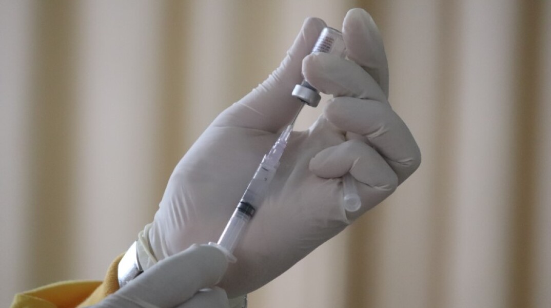 Γιατρός με γάντια μιας χρήσης κρατάει φιάλη με εμβόλιο και σύριγγα©Unsplash/ Mufid Majnun
