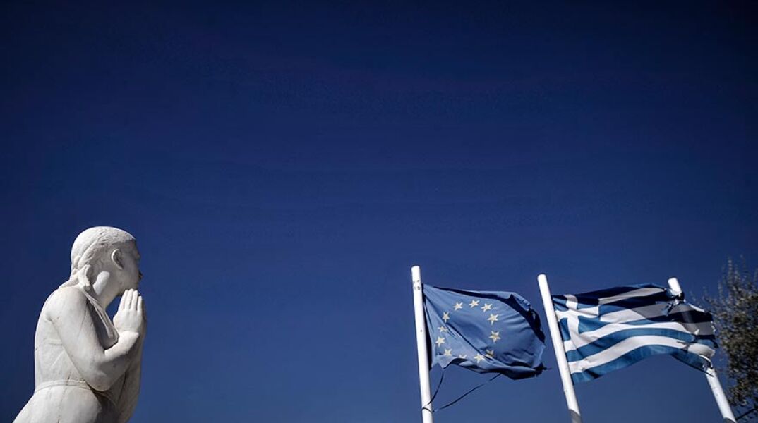 Οι σημαίες της Ελλάδας και της Ευρωπαϊκής Ένωσης κυματίζουν πίσω από το άγαλμα στο Μνημείο Πεσόντων στην Μηλίνα Πηλίου.