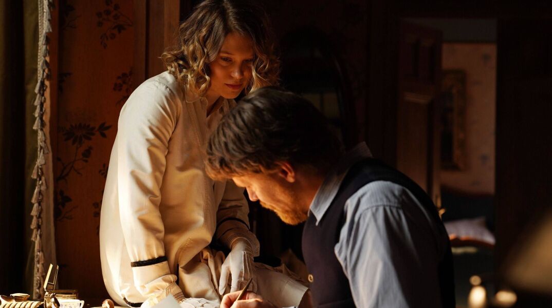 Γυναίκα που κάθεται πάνω σε γραφείο και κοιτά άνδρα που γράφει