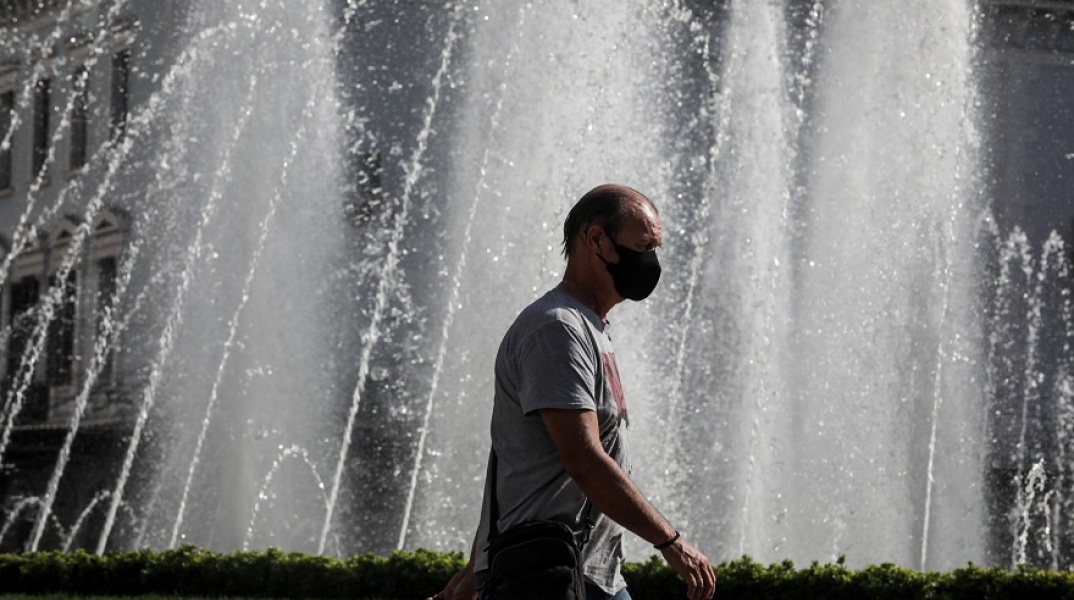 Πολίτης φορά μάσκα προστασίας κατά του κορωνοϊού και περπατά μπροστά από σιντριβάνι