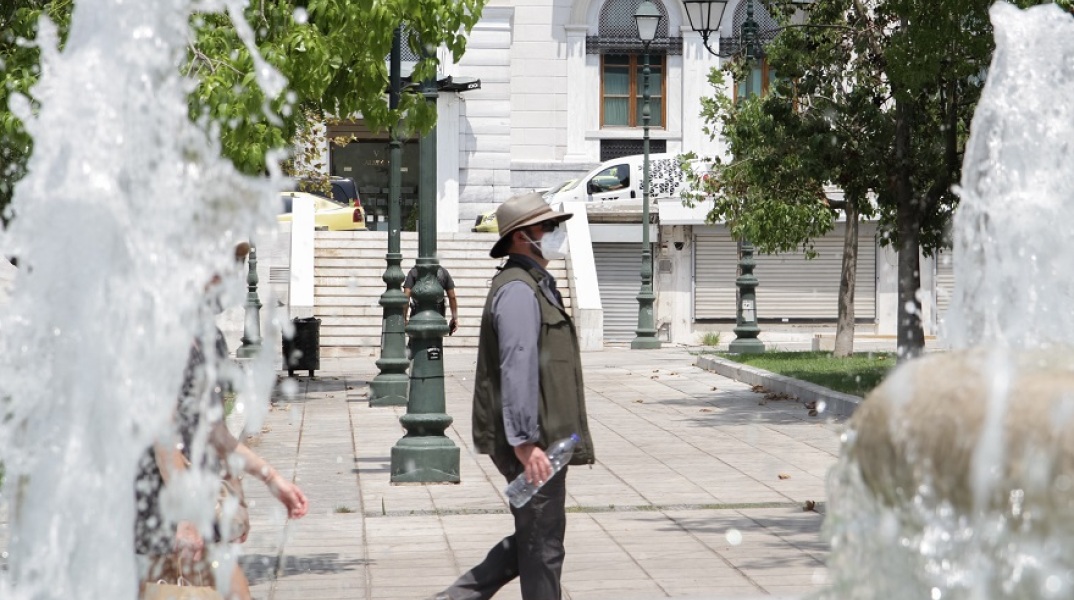Πολίτης φορά τη μάσκα του και το καπέλο του περπατώντας στην πλατεία Συντάγματος