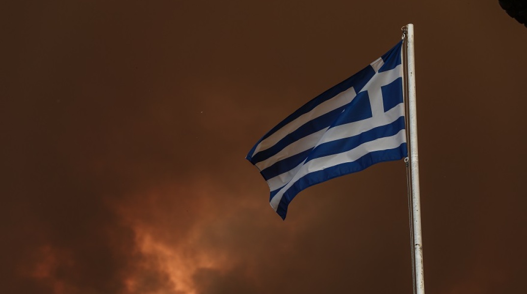 Η ελληνική σημαία με φόντο τον καλυμμένο από καπνό ουρανό στη Βόρεια Εύβοια