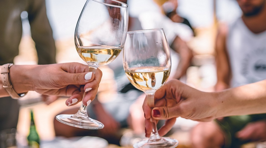 Δυο κορίτσια κρατούν ποτήρια με λευκό κρασί.