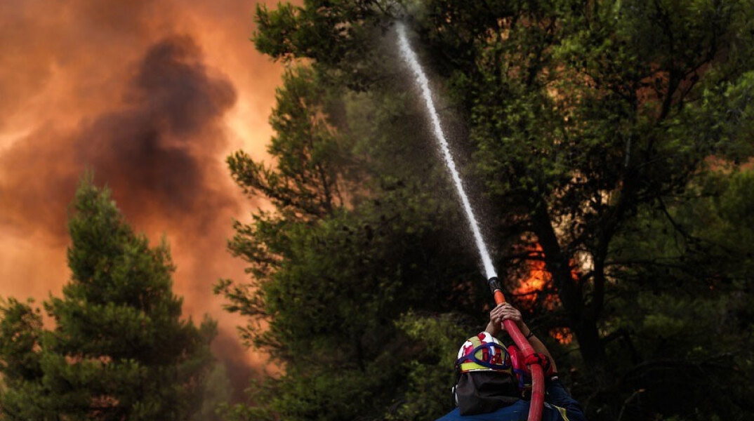 Πυροσβέστης ρίχνει νερό σε δασική πυρκαγιά