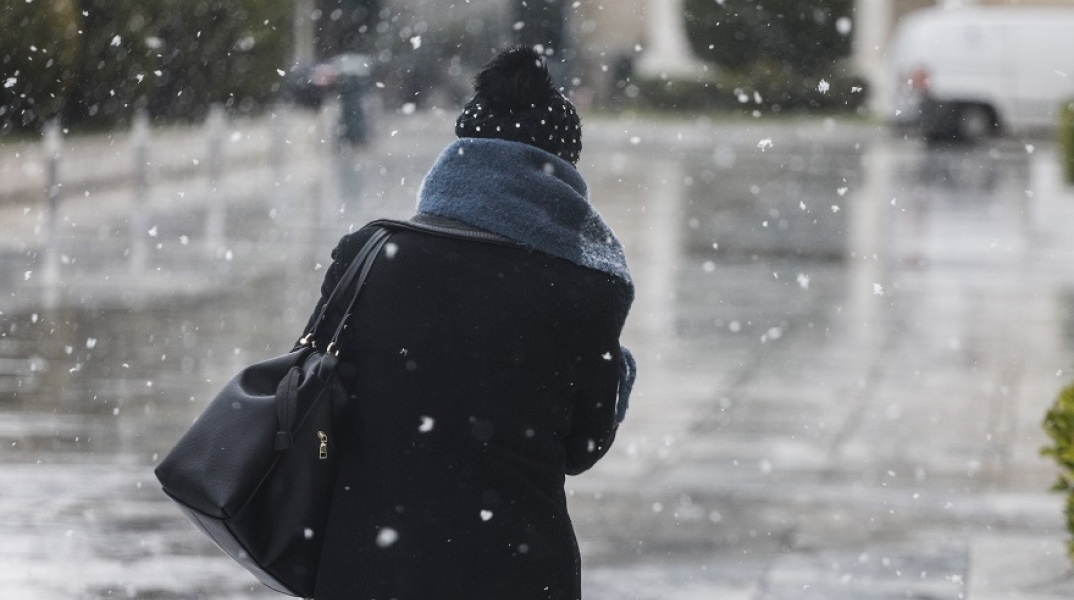 Γυναίκα περπατά στο δρόμο υπό χαμηλές θερμοκρασίες και χιονόπτωση