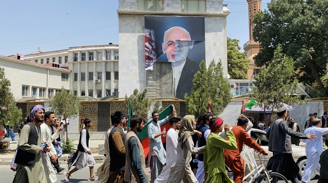 Αφγανοί προσπερνούν την αφίσα του Αφγανού προέδρου Ασράφ Γκανί που εγκατέλειψε τη χώρα μετά την ανάληψη των Ταλιμπάν © EPA / STRINGER