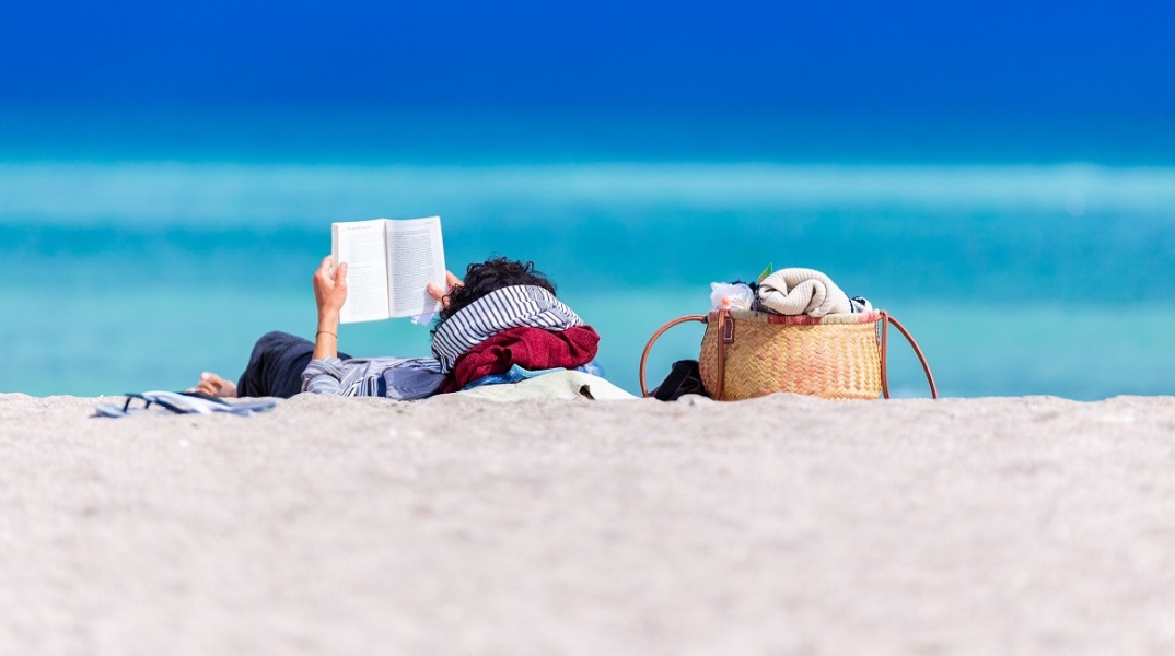 Ένας άνδρας διαβάζει ένα βιβλίο στην παραλία.