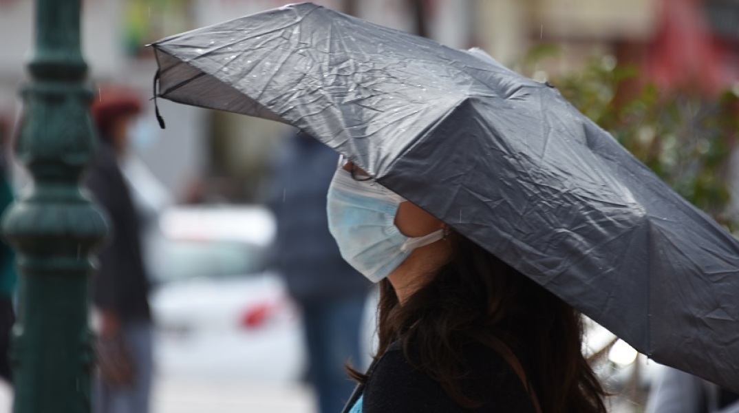 Βροχοπτώσεις - Γυναίκα που φορά μάσκα κρατά την ομπρέλα της