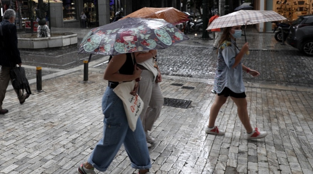 Γυναίκες προστατεύονται από την καταιγίδα κρατώντας ομπρέλα