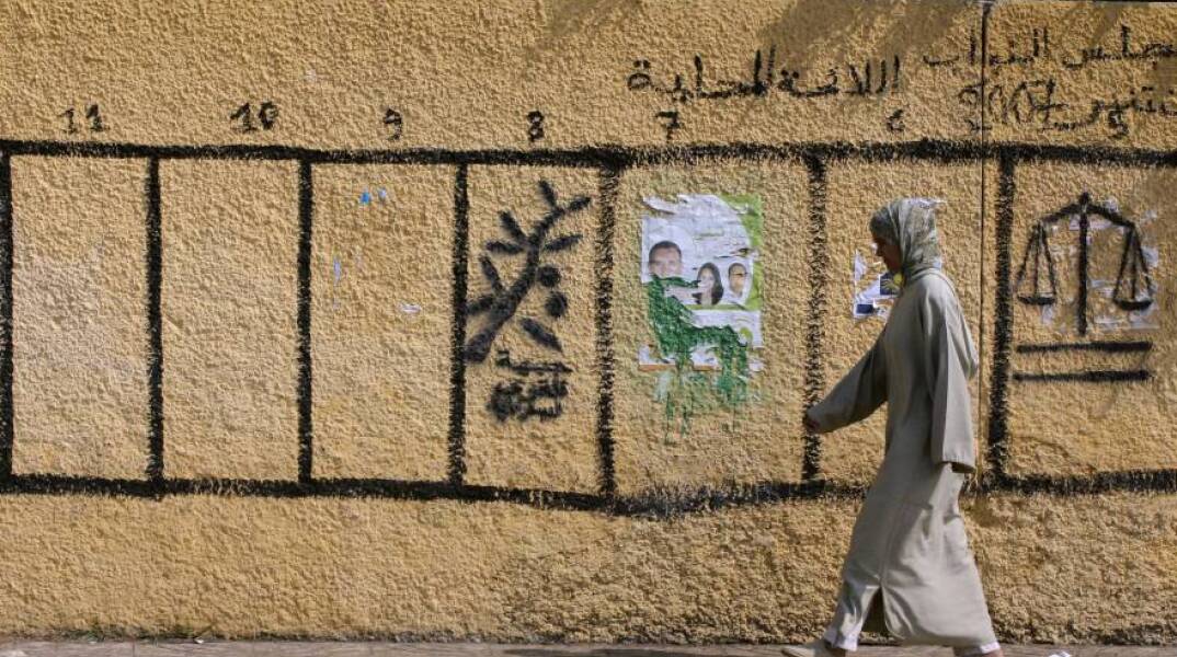 Γυναίκα περπατά στο Ραμπάτ, δίπλα σε έναν τοίχο ζωγραφισμένο με σύμβολα πολιτικών κομμάτων που συμμετέχουν στις βουλευτικές και τοπικές εκλογές στις 8 Σεπτεμβρίου 2021 στο Μαρόκο