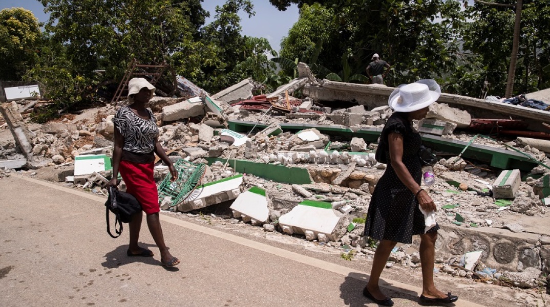 Σεισμός στην Αϊτή: Γυναίκες περπατούν δίπλα σε γκρεμισμένο κτίριο