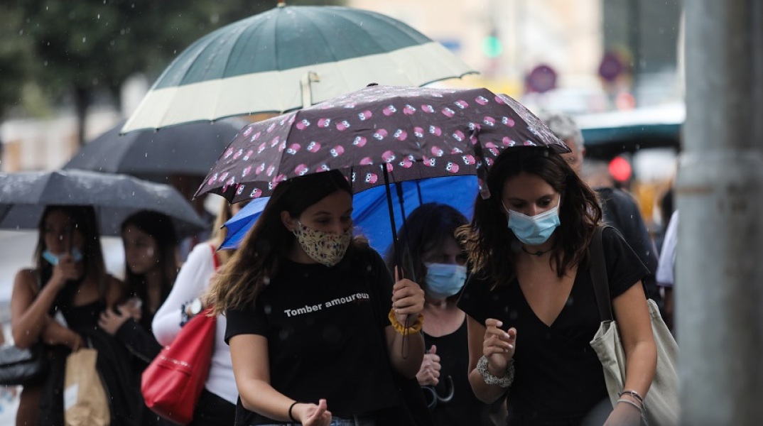 Πολίτες κρατούν ομπρέλα για να προστατευτούν από τον βροχερό καιρό